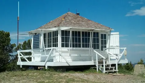 A white wooden fire lookout cabin sits on a mountain peak.