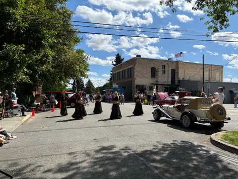 Dancers perform in a street during a community event with classic cars and onlookers.