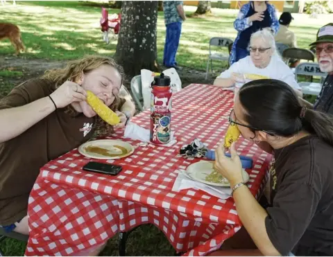 People eating corn on the cob at an outdoor picnic table.