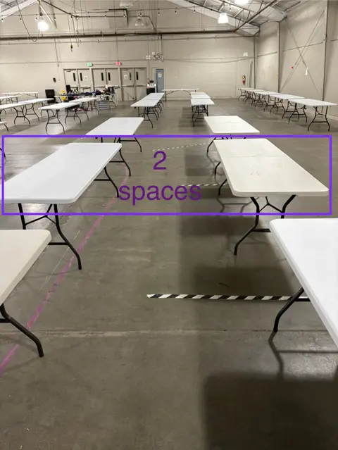 An interior view of a large warehouse space set up with multiple folding tables and text overlayed.