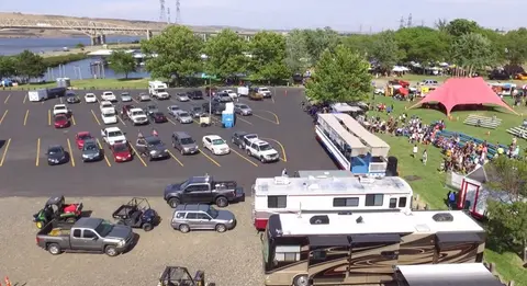 An aerial view of a parking lot and outdoor event with RVs, cars, a large tent, and crowds.
