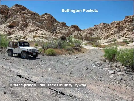 A white off-road vehicle parked on a dirt trail in a rocky desert landscape.