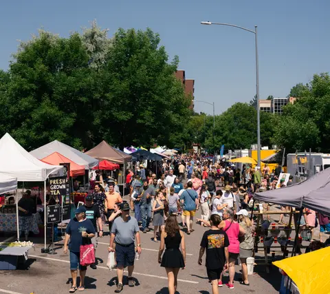 A crowd of people walking through an outdoor street market with tents and food trucks.