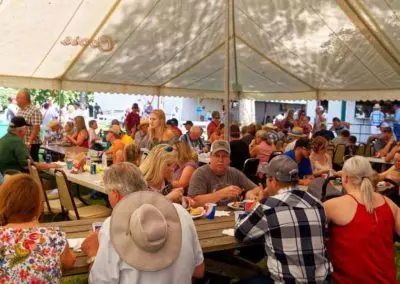A large group of people gather under a tent for a meal or event.