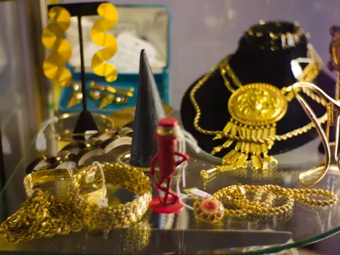 A display case filled with various pieces of gold jewelry and a small red figurine.