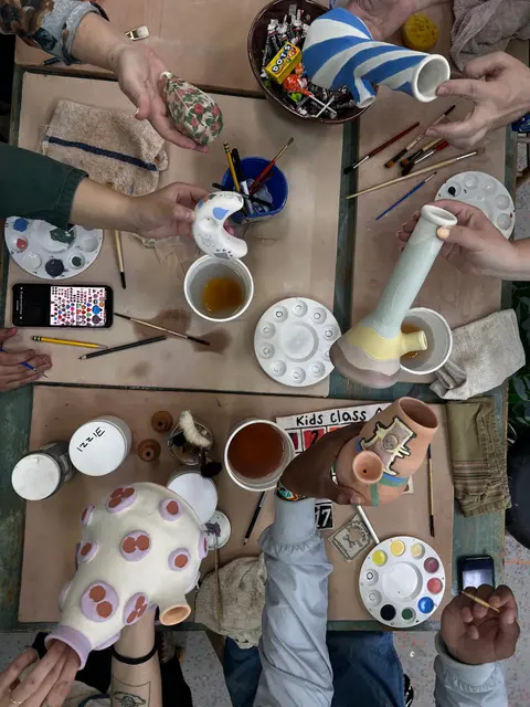 A top-down view of people showing their ceramic art projects around a table.
