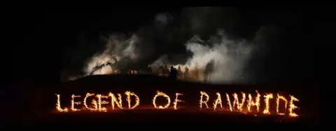 A night view of horse riders silhouetted against smoke and flames with the words LEGEND OF RAWHIDE spelled in fire.