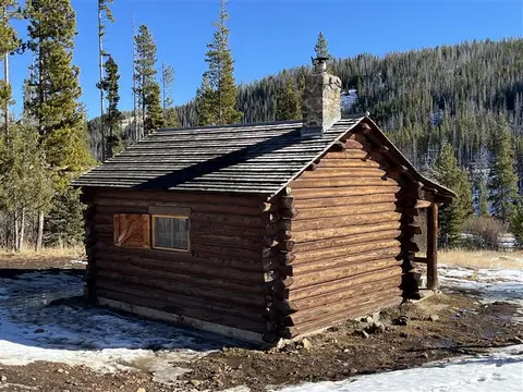 A rustic log cabin stands in a snowy mountainous landscape.