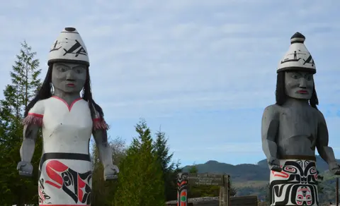 Two large carved wooden figures stand outdoors against a cloudy sky.