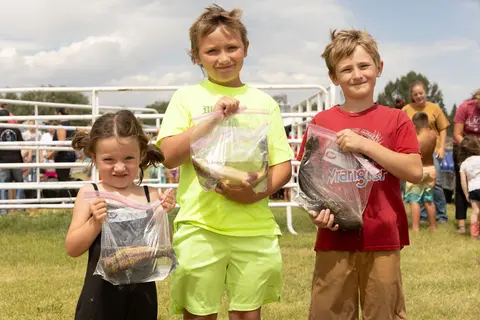 Three children hold up plastic bags containing fish they caught.