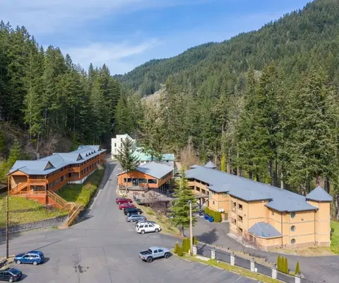 An elevated view of buildings nestled in a forested valley with a parking area.