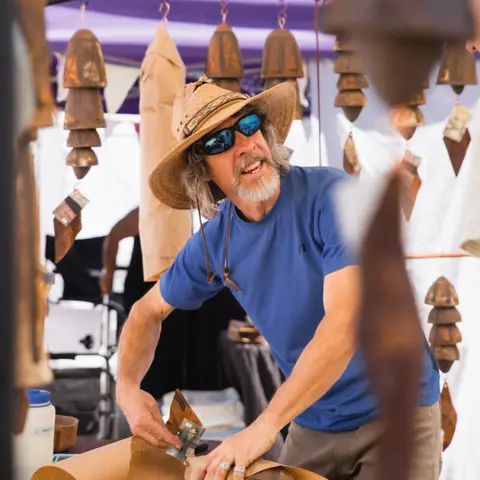 A vendor works at a market booth surrounded by hanging chimes.
