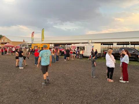 A crowd of people gathers near food trucks at an outdoor event.