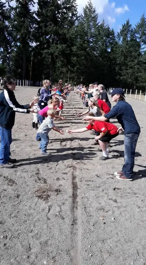 People participating in a long-line game outdoors in a dirt area.