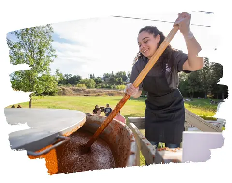 A woman stirs a large pot of food outdoors.