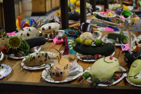Vegetable sculptures are displayed on paper plates on a wooden table.