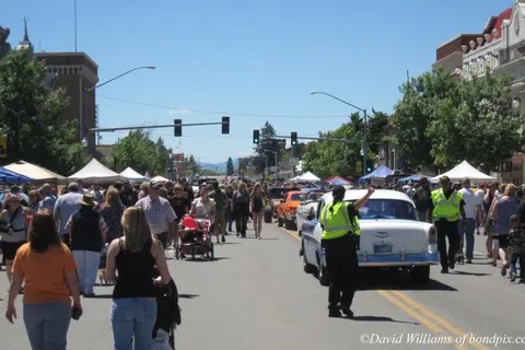 A street filled with crowds and classic cars during an outdoor event.