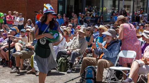 A woman in a costume walks past a seated crowd at an outdoor event.