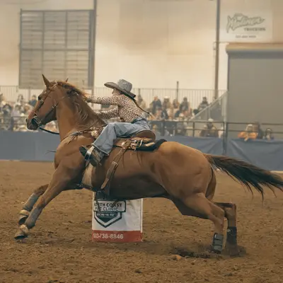 A rider on a horse rounding a barrel in an indoor arena.