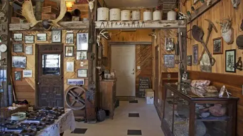 An interior room features wooden walls decorated with historical photos, tools, and taxidermy.