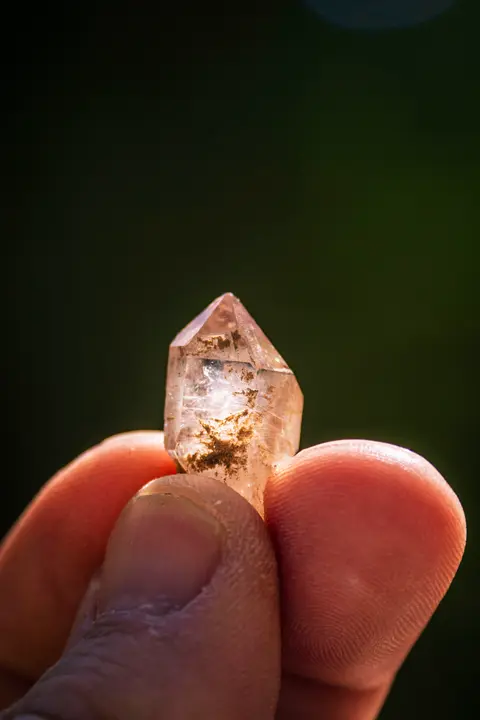 A person holds a small, translucent quartz crystal between their fingers.