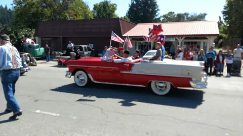 A vintage red and white convertible drives down a street during a parade.
