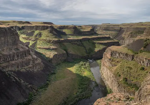 A river flows through a deep rocky canyon under a cloudy sky.
