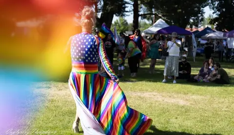 A person in a colorful dress walks through a grassy park during an outdoor event.