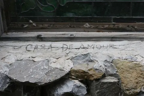 A stone wall beneath a window features the words CASA DE AMOUR carved into the plaster.