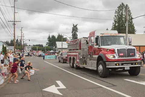 A fire truck participates in a parade on a street lined with onlookers.