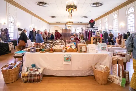 People browse a craft fair inside a large hall with high ceilings.