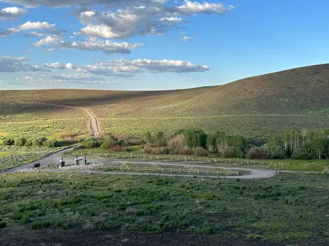 A dirt road winds through rolling green hills under a blue sky with scattered clouds.