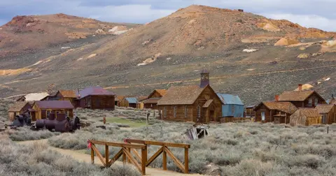 An old wooden ghost town sits in a desert valley beneath barren hills.