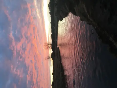 A sunset sky reflects on a body of water next to land.