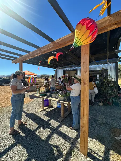 People gather under a shaded pavilion at an outdoor market.