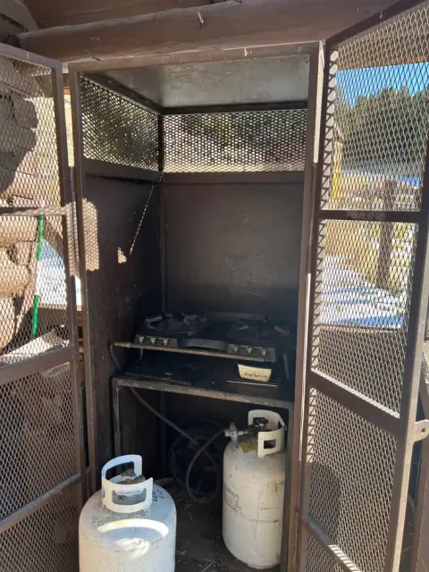 A metal cabinet with mesh doors containing a stove and propane tanks.