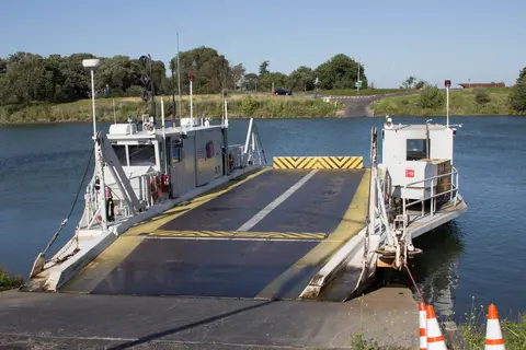 A ferry boat sits at the water's edge with its ramp lowered.