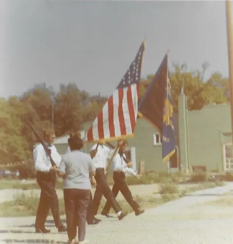 A color photograph of people carrying flags outdoors.