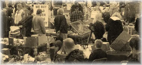 A crowd of people browsing tables at an indoor market or antique fair.