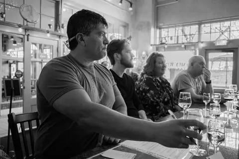 A black and white photo of people seated at a bar tasting wine.
