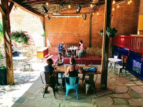 People sit at tables in an outdoor patio dining area with exposed brick walls and string lights.