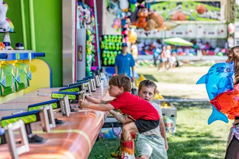 Two young boys play a carnival game outdoors.
