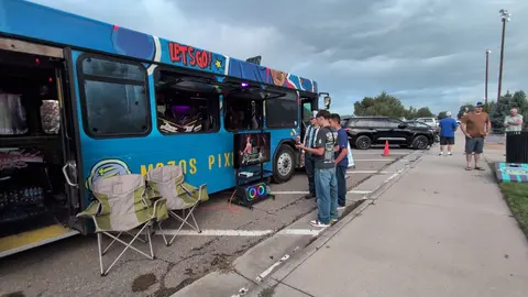 People playing a video game setup outside a decorated bus in a parking lot.