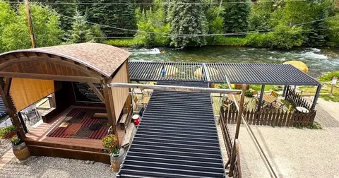 An outdoor stage and patio seating area situated alongside a river.