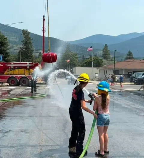 People and children use a fire hose to spray water during an outdoor community event.