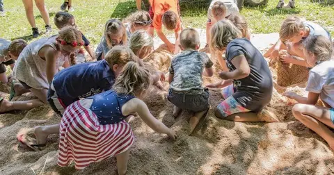 Children play and dig in a large pile of sawdust.