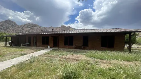 A single-story brick building with a metal roof under a cloudy sky in a mountainous landscape.