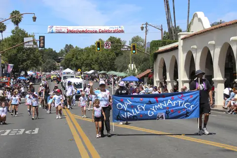 A street parade with participants carrying a banner and spectators watching.