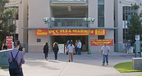 People walk toward the entrance of a building with flea market banners.