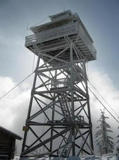 A tall wooden fire lookout tower stands outdoors in a snowy landscape.